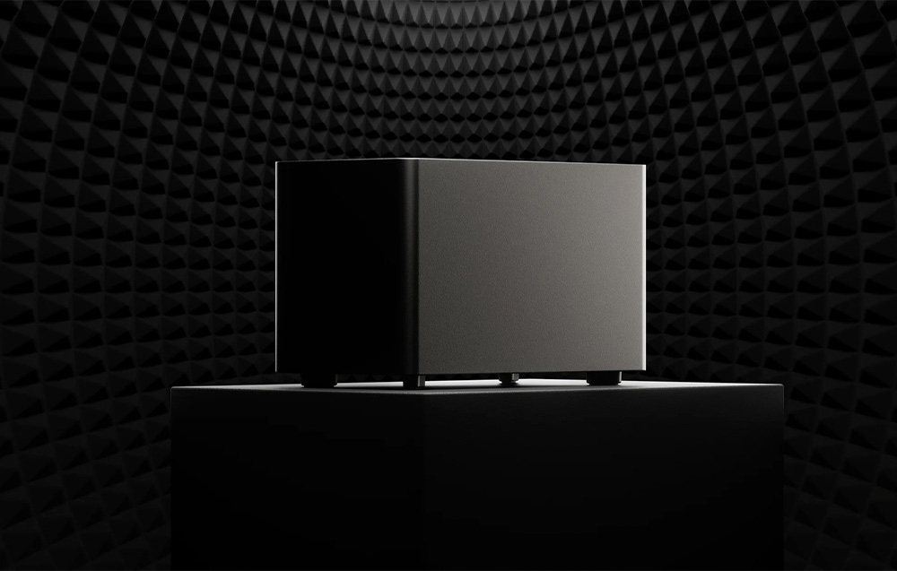 Subwoofer Ultimea σε σκούρο φόντο με ηχοαπορροφητικά πάνελ, τοποθετημένο σε υπερυψωμένη πλατφόρμα