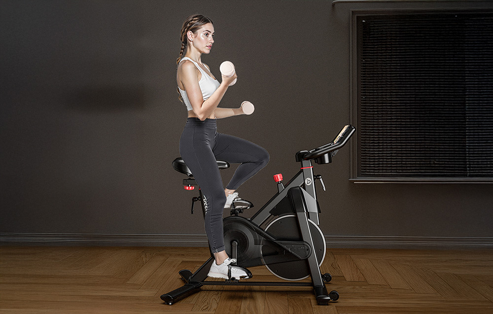 Άτομο που γυμνάζεται σε μαύρο ποδήλατο spinning κρατώντας ελαφριά αλτήρες και στα δύο χέρια