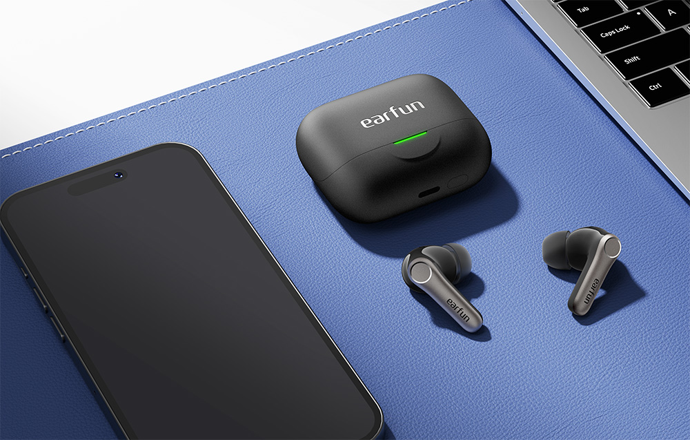 Μαύρα ακουστικά EarFun με θήκη, smartphone και φορητό υπολογιστή σε μπλε επιφάνεια γραφείου