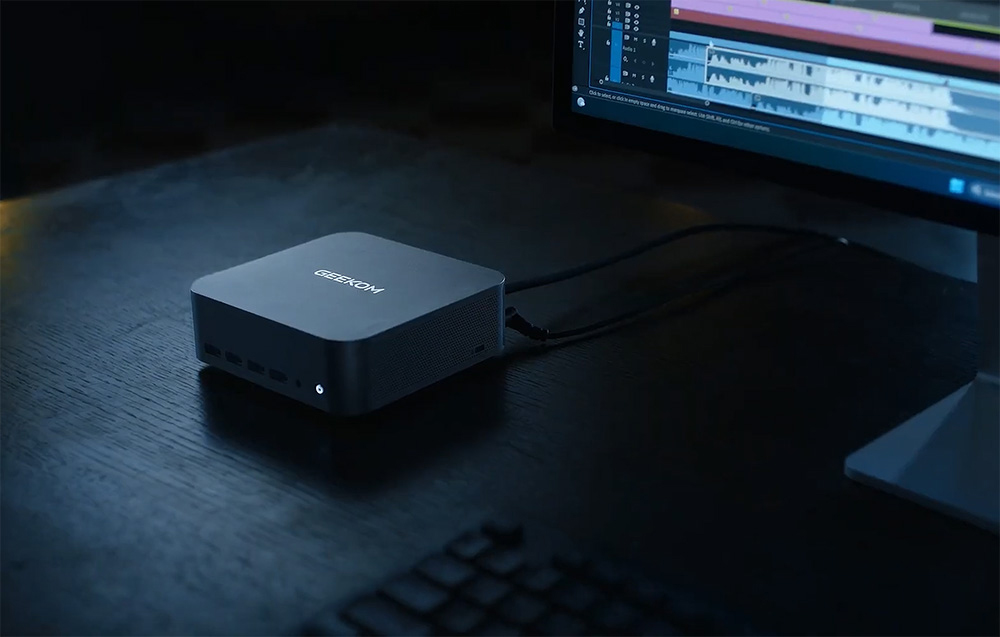 Geekom MINI PC σε γραφείο δίπλα σε οθόνη σε σκοτεινό δωμάτιο