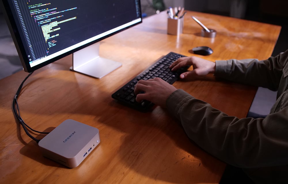 Geekom mini PC συνδεδεμένο σε οθόνη σε ξύλινο γραφείο