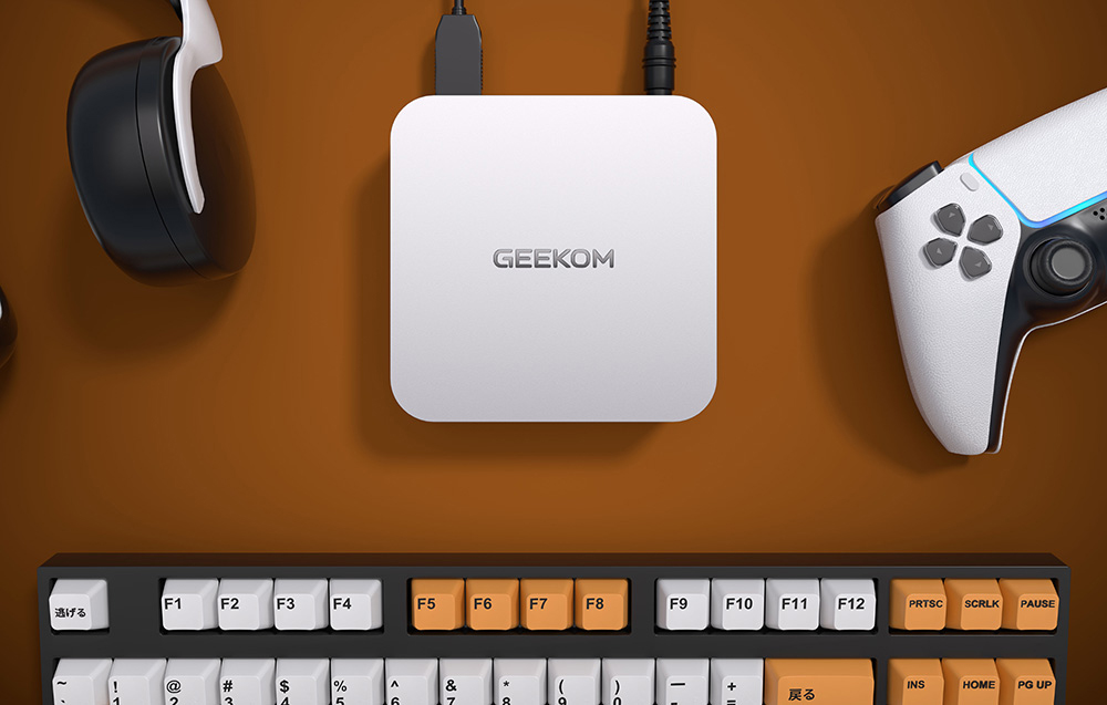 Mini PC Geekom σε γραφείο δίπλα σε χειριστήριο παιχνιδιών, πληκτρολόγιο και ακουστικά