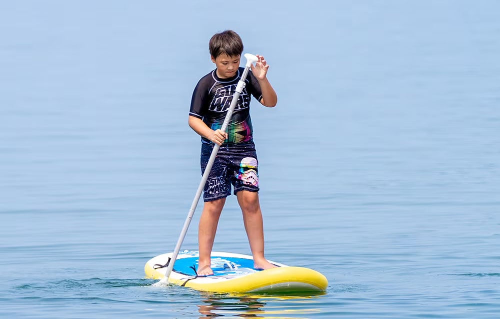 Αγόρι σε σανίδα σέρφινγκ με κουπί στο χέρι