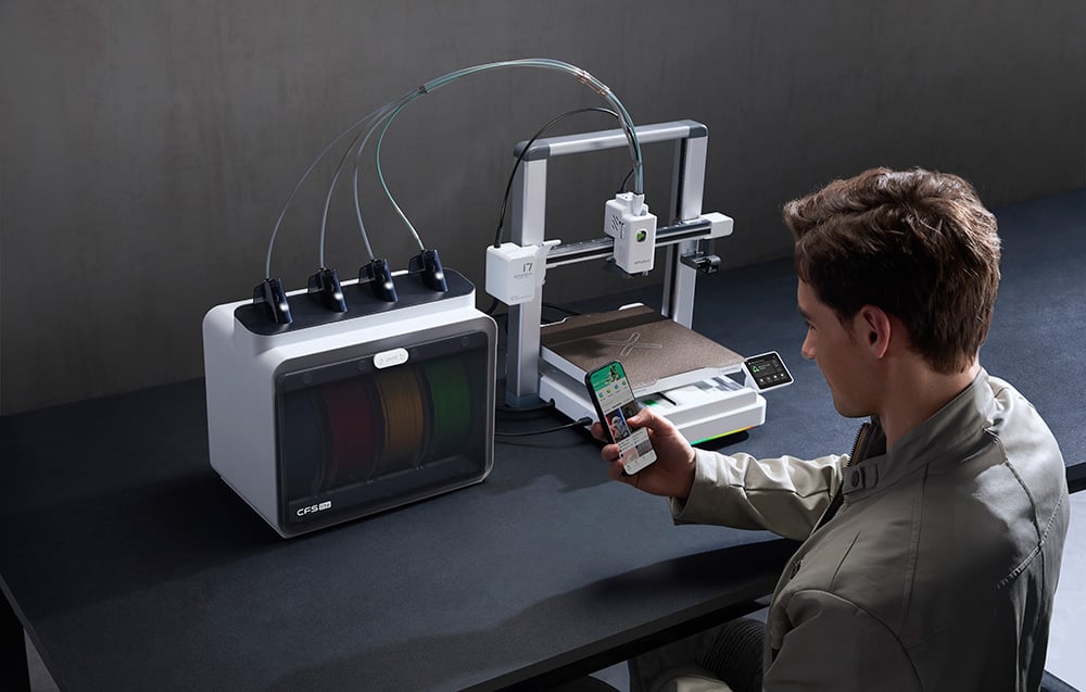Ένας άνδρας χειρίζεται έναν εκτυπωτή 3D με ένα smartphone σε ένα σκοτεινό δωμάτιο.