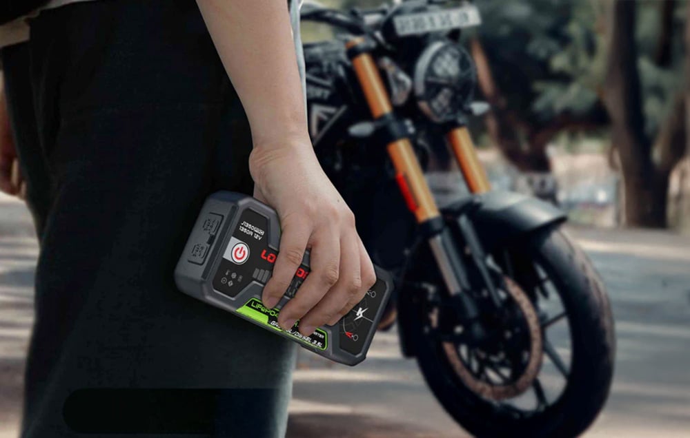 Ένα χέρι που κρατά το συμπαγές LOKITHOR jump starter με φόντο μια σταθμευμένη μοτοσικλέτα.