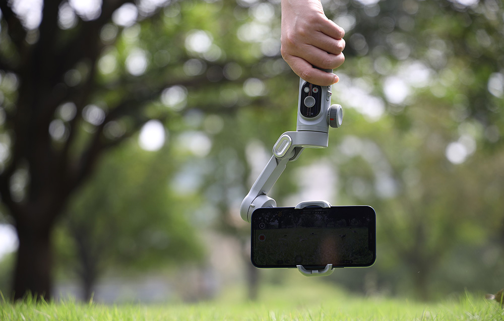 Ένα gimbal με ένα smartphone κρατημένο πάνω από το γρασίδι κατά τη διάρκεια της καταγραφής σε εξωτερικό χώρο.
