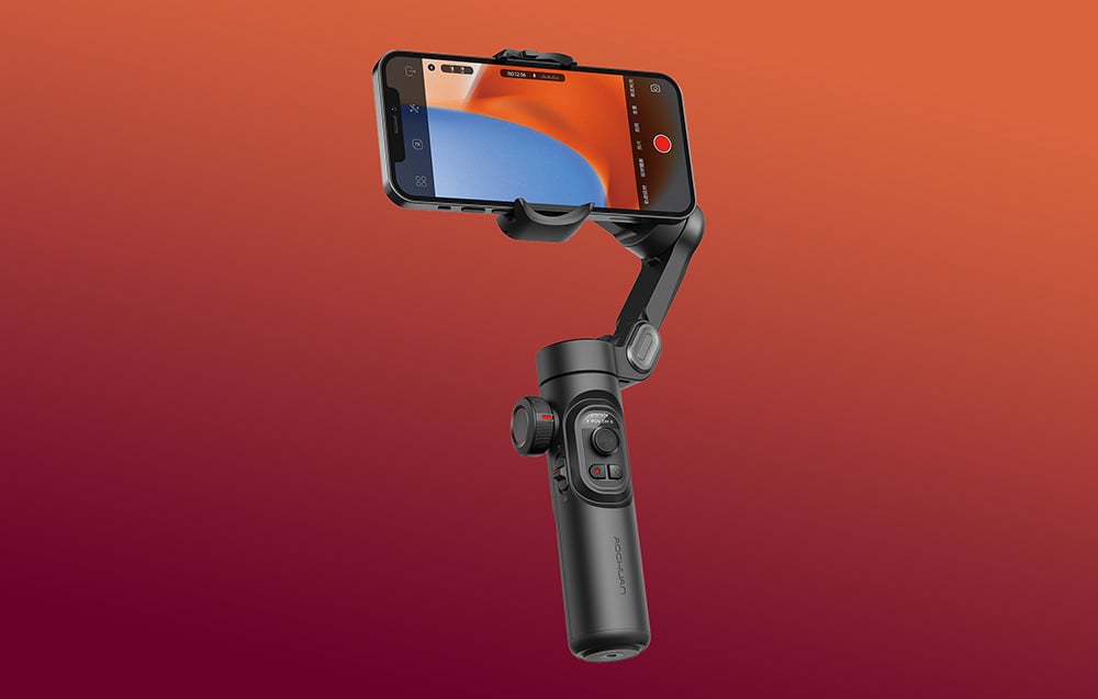 Ένα gimbal με smartphone σε λειτουργία εγγραφής, τοποθετημένο μπροστά από φόντο με κόκκινο-πορτοκαλί ντεγκραντέ.