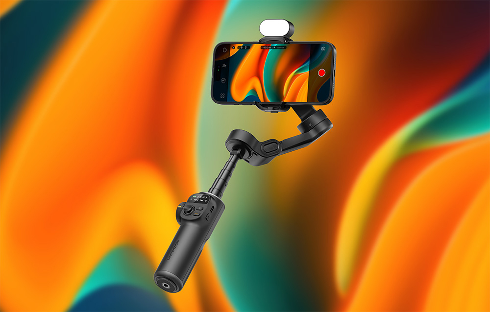 Ένα μαύρο gimbal με ένα smartphone και ενσωματωμένο φως μπροστά από ένα πολύχρωμο φόντο με αποχρώσεις του πορτοκαλί και του πράσινου.
