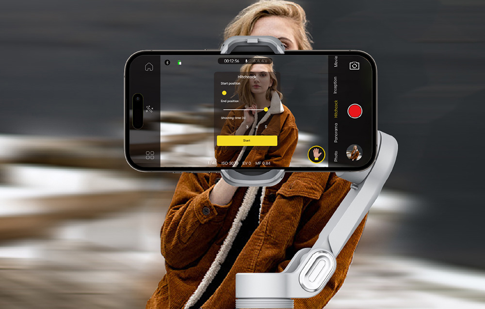 Ένα gimbal με smartphone που δείχνει τη διεπαφή ενώ βιντεοσκοπεί μια γυναίκα με καφέ μπουφάν.