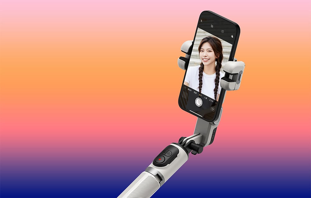 Ένα gimbal σε βραχίονα επέκτασης με ένα smartphone που εμφανίζει μια selfie μιας χαμογελαστής γυναίκας μπροστά από πορτοκαλί φόντο.