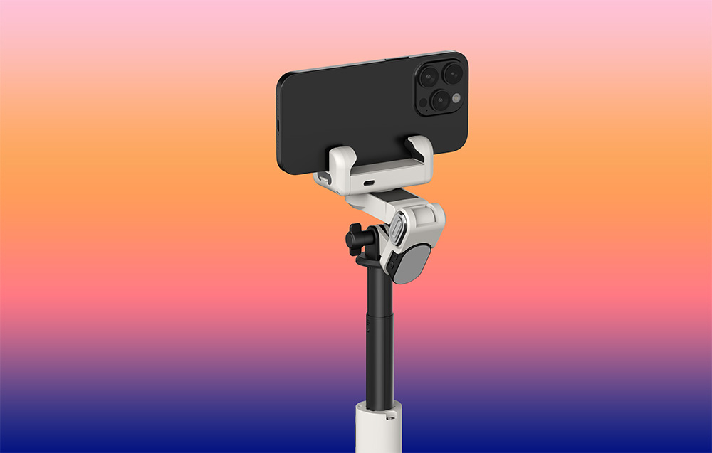 Ένα gimbal με ένα smartphone, όπως φαίνεται από πίσω, τοποθετημένο σε έναν βραχίονα επέκτασης μπροστά από ένα φόντο με χρωματική διαβάθμιση.