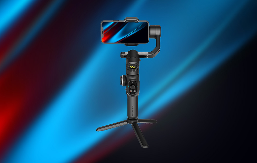 Ένα μαύρο gimbal με ένα smartphone τοποθετημένο οριζόντια σε ένα μίνι τρίποδο πάνω σε ένα σκούρο μπλε φόντο.