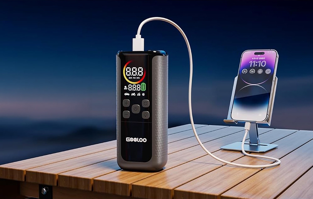 Φορητός συμπιεστής GOOLOO που φορτίζει ένα smartphone μέσω καλωδίου USB πάνω σε ξύλινο τραπέζι