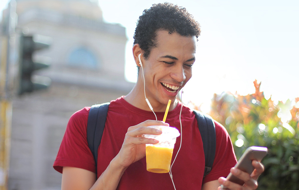 Ένας χαμογελαστός άνδρας που κρατά ένα smartphone και ένα ποτήρι χυμό
