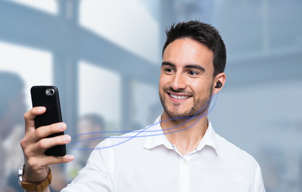 Ένας χαμογελαστός άνδρας κρατά ένα smartphone και χρησιμοποιεί ασύρματα ακουστικά.