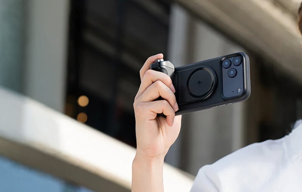 Ένα χέρι που κρατά ένα smartphone με μαύρη βάση στήριξης ενώ τραβάει φωτογραφία σε εξωτερικό χώρο