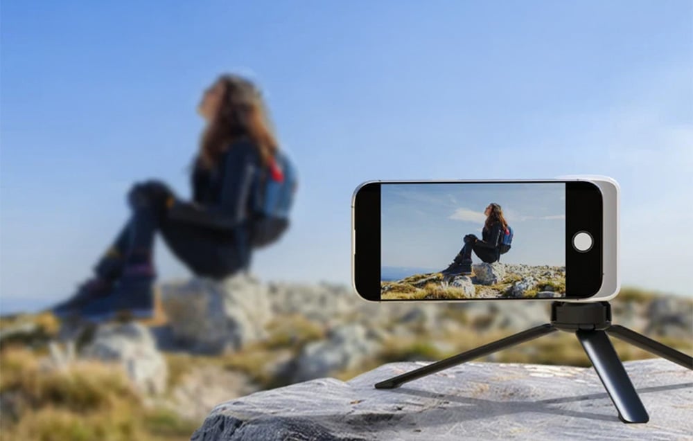 Ένα smartphone σε τρίποδο που καταγράφει ένα άτομο που κάθεται σε ένα βράχο σε εξωτερικό χώρο