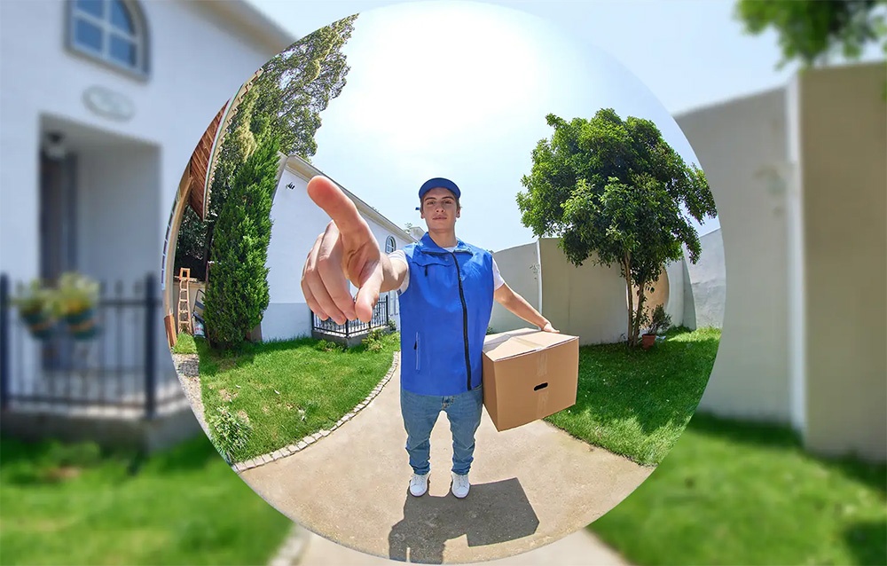 Προβολή από κάμερα fish-eye ενός ταχυδρόμου με μπλε γιλέκο που κρατά ένα πακέτο και δείχνει με το δάχτυλό του προς τον φακό