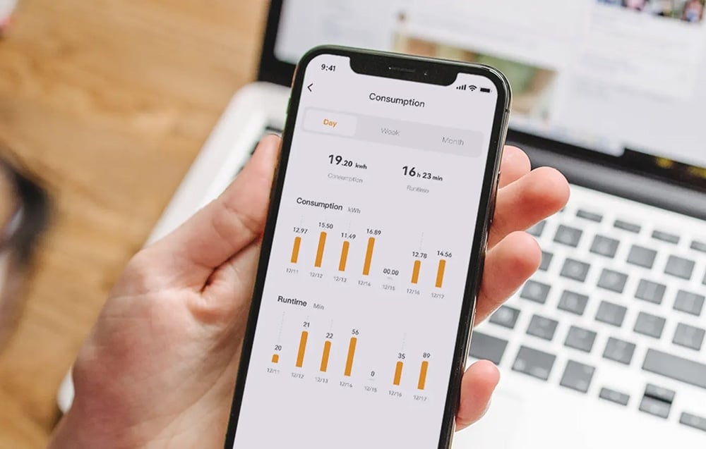 Ένα χέρι που κρατά ένα smartphone με την εφαρμογή Consumption να εμφανίζει γραφήματα κατανάλωσης ηλεκτρικού ρεύματος και χρόνου λειτουργίας