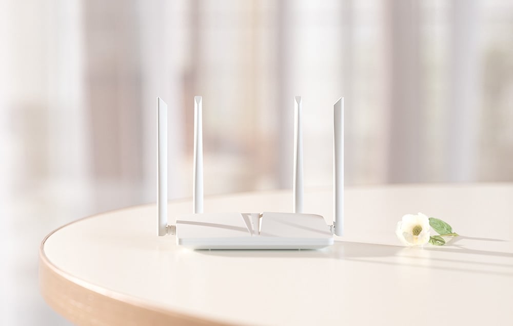 Ένας λευκός δρομολογητής Wi-Fi με τέσσερις κεραίες βρίσκεται πάνω σε ένα ανοιχτόχρωμο στρογγυλό τραπέζι δίπλα σε ένα λευκό λουλούδι με φόντο ένα θολωμένο εσωτερικό