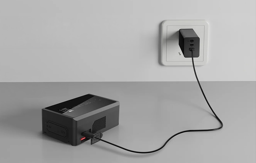 Μια μπαταρία Neewer συνδεδεμένη μέσω καλωδίου USB σε έναν μαύρο μετασχηματιστή ρεύματος, ο οποίος είναι συνδεδεμένος σε μια λευκή πρίζα.