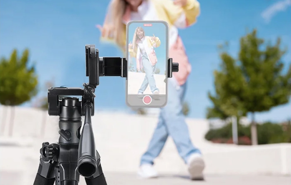Ένα smartphone τοποθετημένο σε τρίποδο καταγράφει μια γυναίκα που ποζάρει σε εξωτερικό χώρο