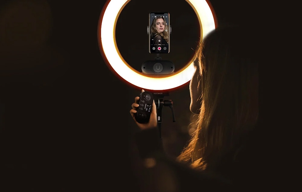 Γυναίκα που καταγράφει με ένα smartphone τοποθετημένο σε ένα δακτυλιοειδές φως και κρατά ένα τηλεχειριστήριο
