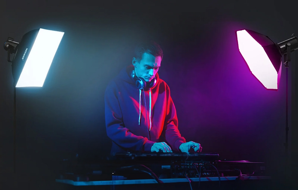Ένας DJ που παίζει στην κονσόλα, φωτισμένος από τα πλάγια από δύο φωτιστικά με μπλε και μοβ φως.