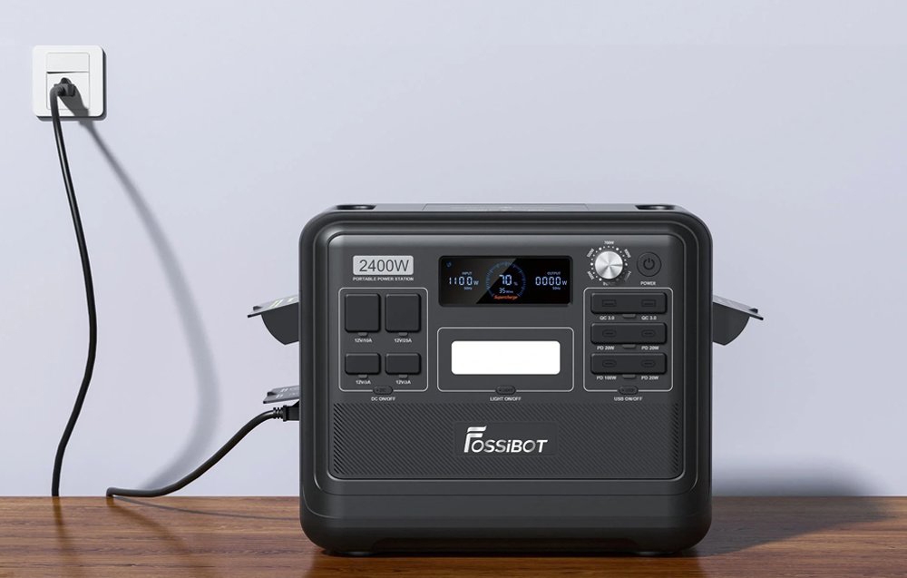 Μαύρος σταθμός τροφοδοσίας Fossibot 2400W συνδεδεμένος σε πρίζα τοίχου πάνω σε ξύλινο γραφείο