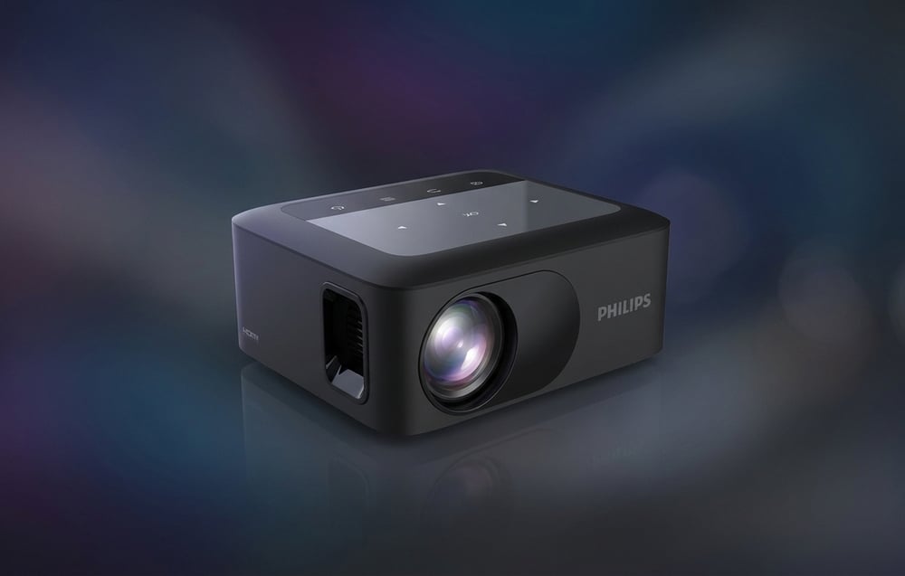 Ένας μαύρος προβολέας PHILIPS με την ένδειξη «HDMI» στο πλάι, τοποθετημένος πάνω σε σκούρο, θολό φόντο με σημεία φωτός