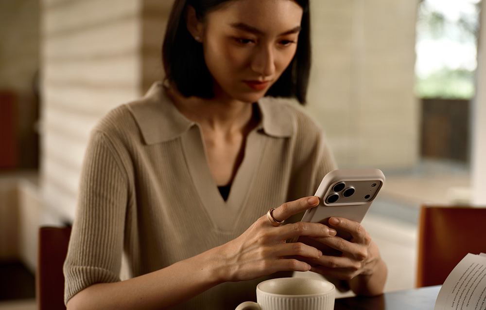 Μια γυναίκα που κρατά ένα smartphone και με τα δύο χέρια, επιδεικνύοντας ένα έξυπνο δαχτυλίδι από ροζ χρυσό στο δάχτυλό της