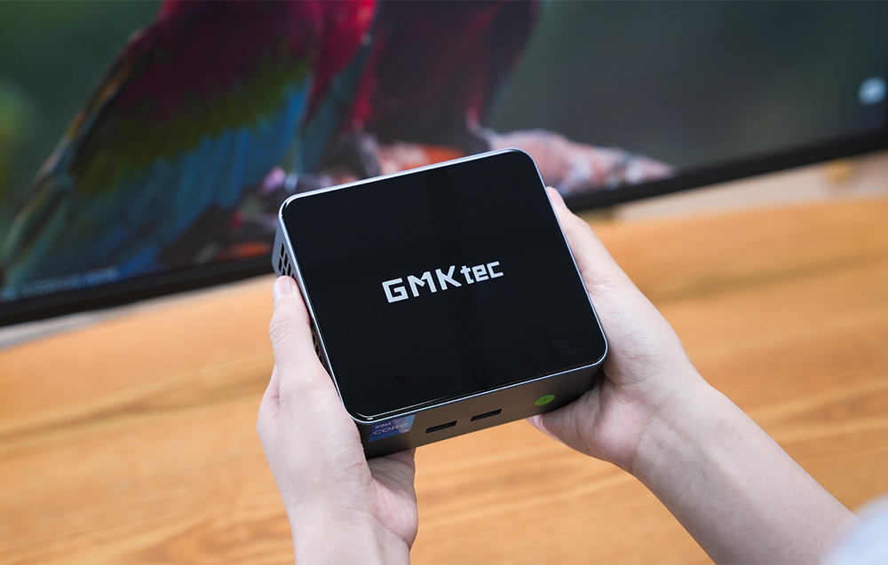 Ο μίνι υπολογιστής GMKtec M3 Pro στα χέρια με φόντο μια οθόνη