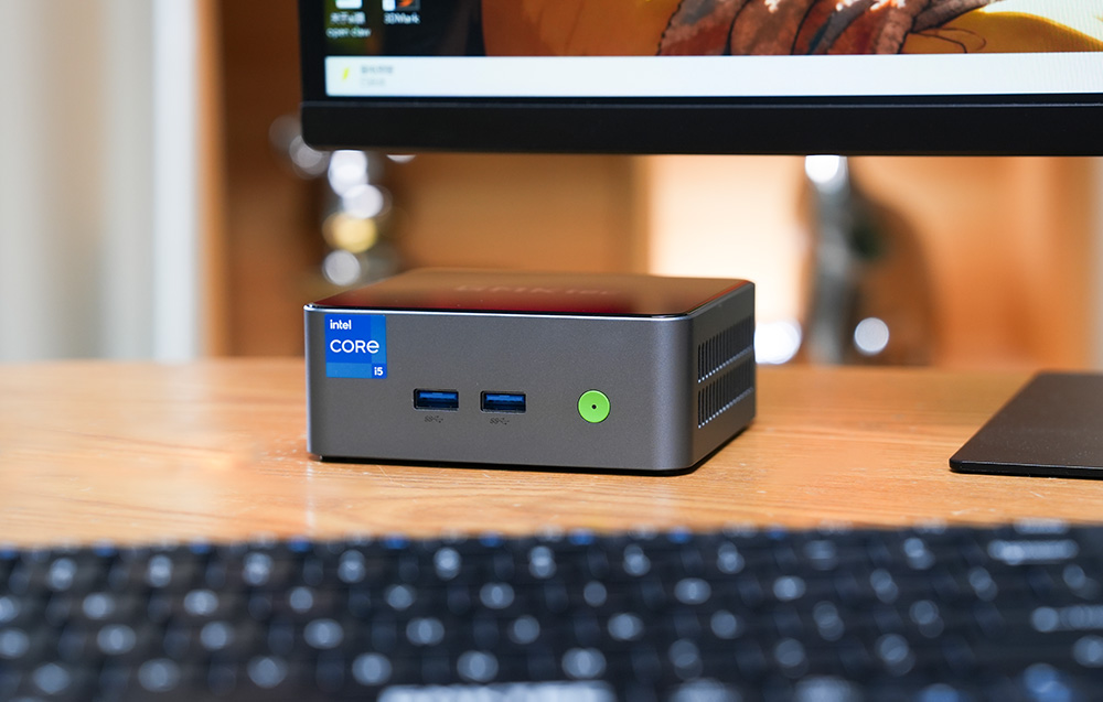 Το GMKtec M3 Pro Mini PC τοποθετημένο σε ένα γραφείο κάτω από μια οθόνη, έτοιμο για καθημερινή εργασία και ψυχαγωγία.