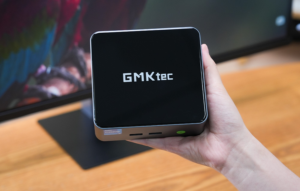 Ο συμπαγής υπολογιστής GMKtec M3 Pro κρατημένος στο χέρι με φόντο μια οθόνη