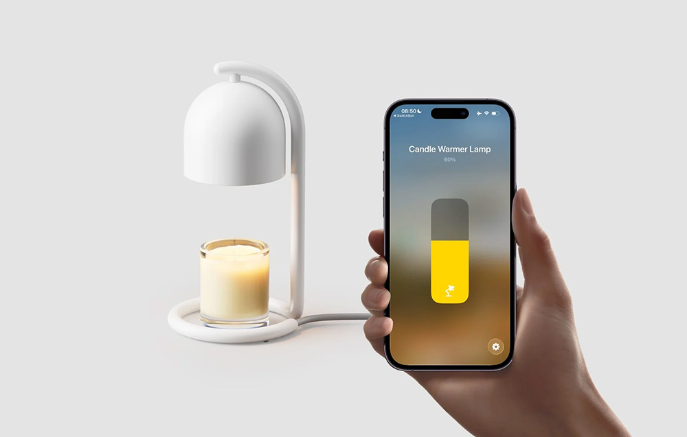 Ένα χέρι που κρατά ένα smartphone με την εφαρμογή SwitchBot, όπου εμφανίζεται ένα ρυθμιστικό ρυθμισμένο στο 60%, με ένα λευκό θερμαντικό κεριών και ένα αρωματικό κερί σε γυάλινο δοχείο στο φόντο.