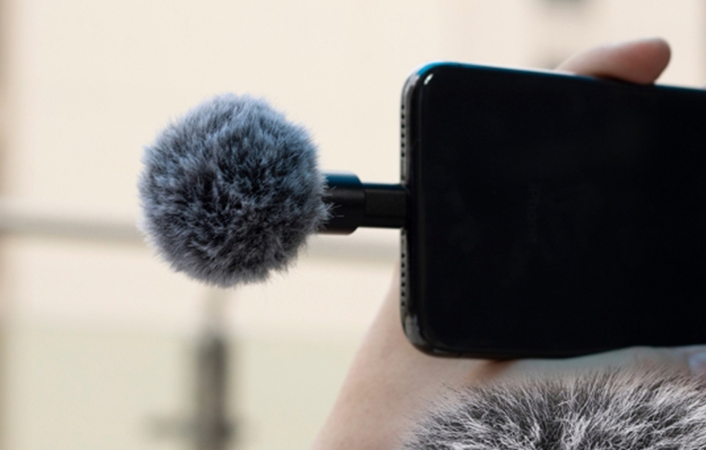 Smartphone στο χέρι με ένα μικρό μικρόφωνο προσαρτημένο, με γούνα ως αντιανεμικό