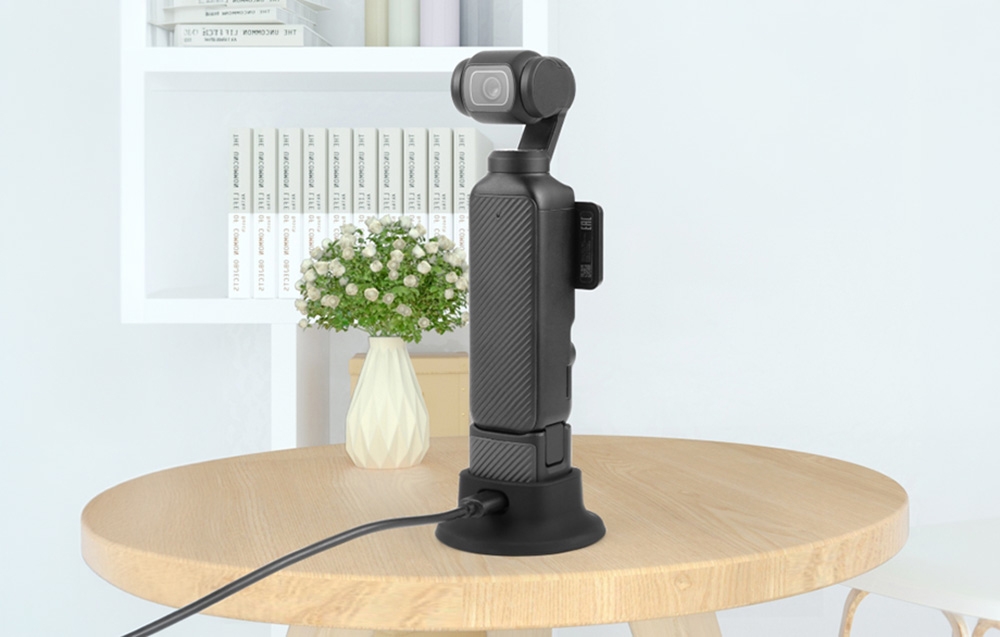 Κάμερα DJI Osmo Pocket 3 τοποθετημένη σε μαύρη βάση σιλικόνης πάνω σε ξύλινο τραπέζι σε φωτεινό δωμάτιο.