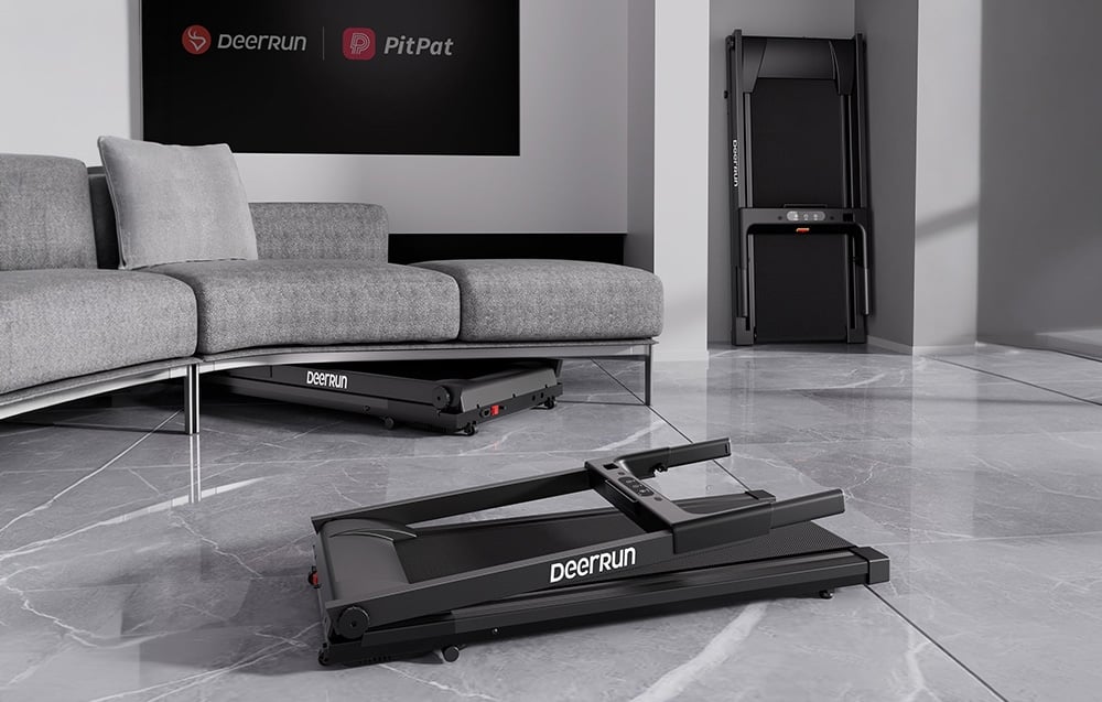 Ένας διπλωμένος διάδρομος DeerRun είναι αποθηκευμένος σε οριζόντια θέση κάτω από έναν γκρι καναπέ, ενώ ένας άλλος στέκεται όρθιος στη γωνία του σαλονιού.