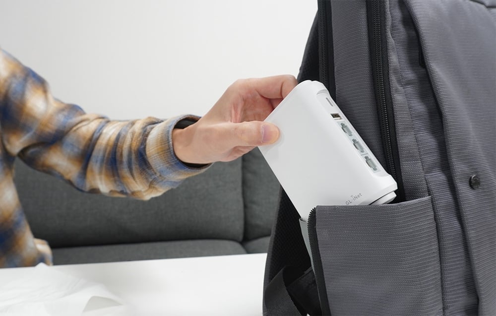 Ένας λευκός δρομολογητής GL.iNet τοποθετείται μέσα σε ένα γκρι σακίδιο