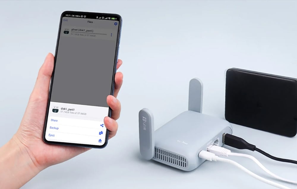 Ένα smartphone κρατιέται στο χέρι· στο βάθος, ένας δρομολογητής βρίσκεται πάνω σε ένα μικρό τραπέζι