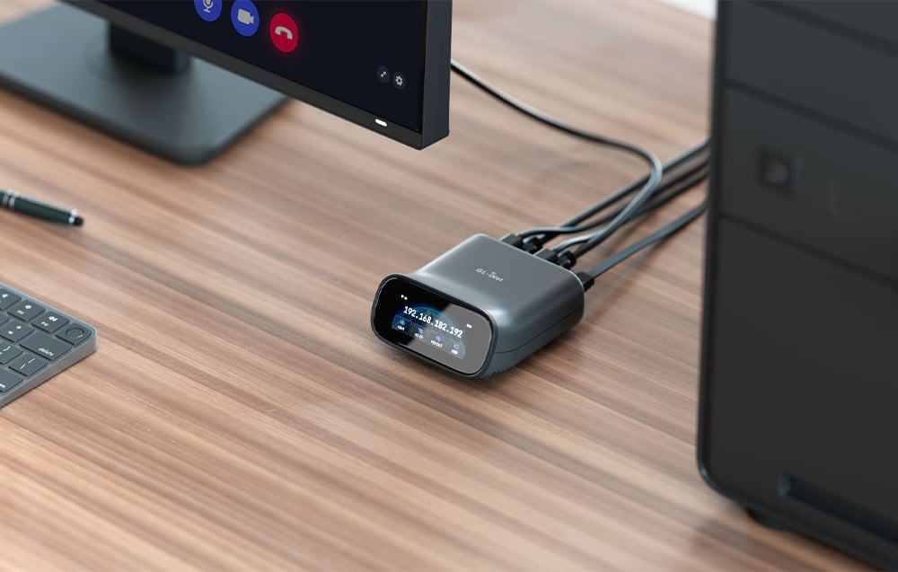 Ένας διακόπτης KVM συνδεδεμένος με καλώδια πάνω σε ένα γραφείο· δίπλα του βρίσκεται ένας επιτραπέζιος υπολογιστής και μια οθόνη με εξοπλισμό τηλεδιάσκεψης