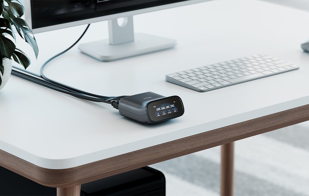 Ένας διακόπτης KVM με την IP διεύθυνσή του εμφανισμένη βρίσκεται πάνω σε ένα λευκό γραφείο δίπλα σε ένα επίπεδο πληκτρολόγιο, κάτω από μια οθόνη.