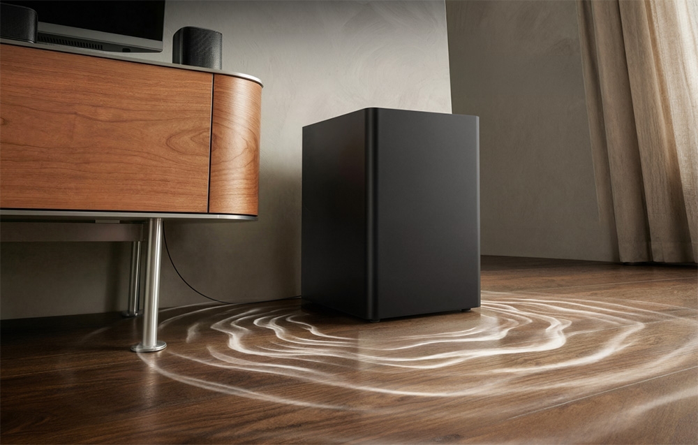 Ένα μαύρο subwoofer σε ξύλινο πάτωμα δίπλα σε μια καφέ συρταριέρα