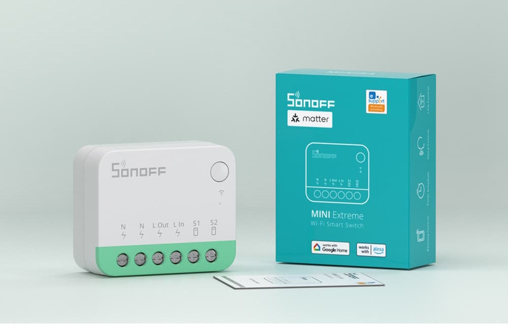Ένας λευκός και πράσινος διακόπτης Sonoff δίπλα στο εγχειρίδιο χρήσης και τη συσκευασία, σε ανοιχτόχρωμο φόντο