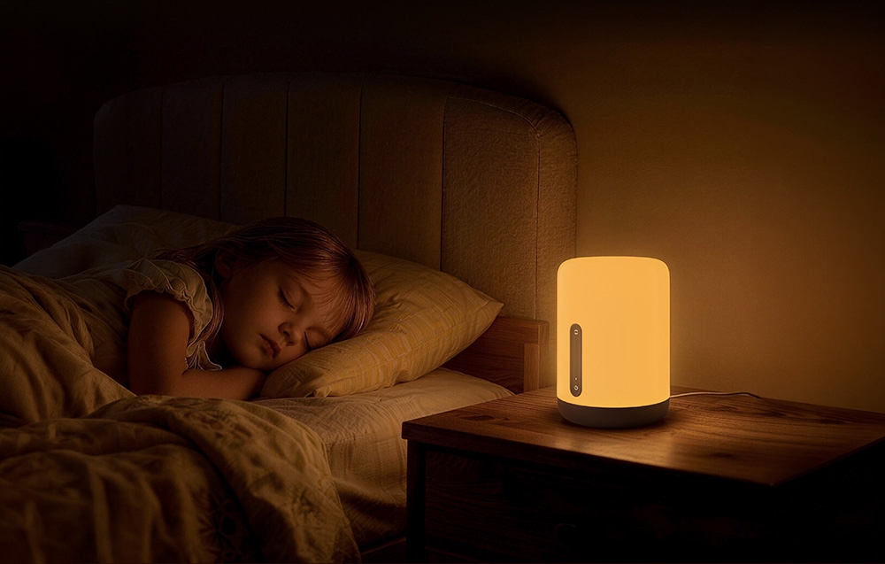 Ένα παιδί που κοιμάται στο κρεβάτι, δίπλα στο οποίο ένα νυχτερινό φως ρίχνει μια ζεστή λάμψη πάνω σε ένα ξύλινο κομοδίνο