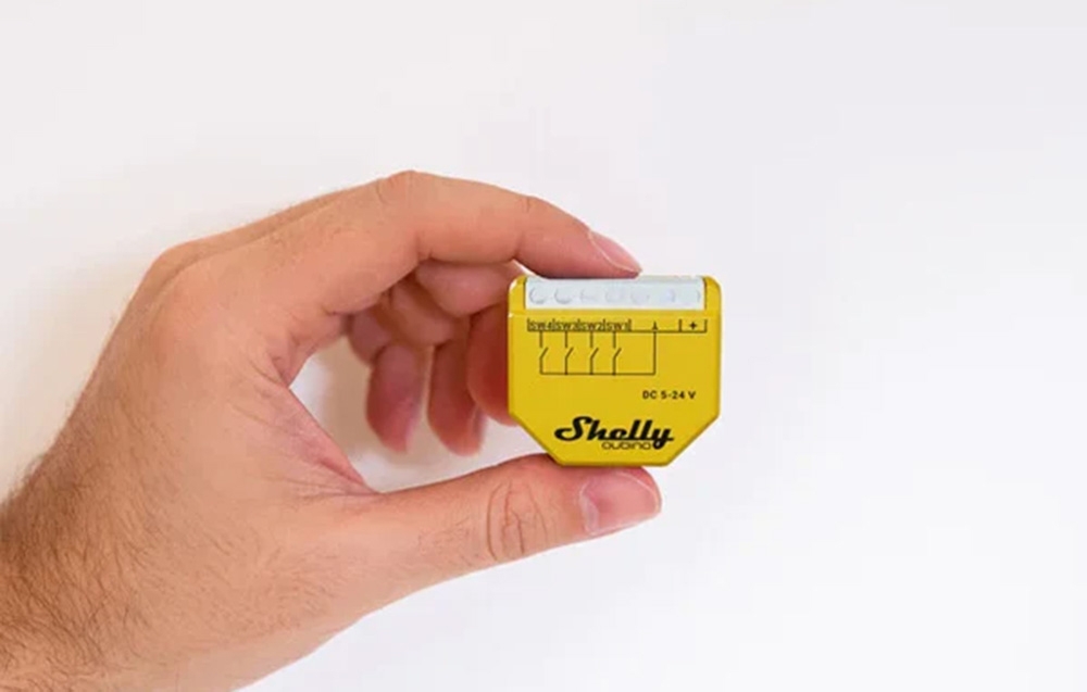 Ένα άτομο που κρατά έναν κίτρινο διακόπτη Shelly με φόντο λευκό.