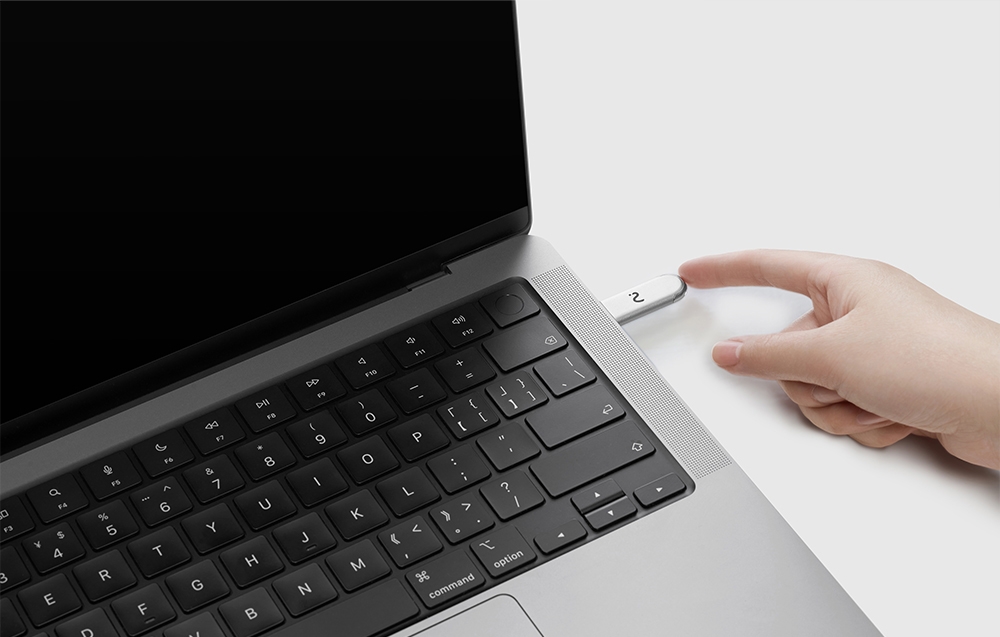 Ένα δάχτυλο αγγίζει το μεταλλικό dongle με πράσινο LED, το οποίο είναι συνδεδεμένο στο πλάι ενός ανοιχτού φορητού υπολογιστή.