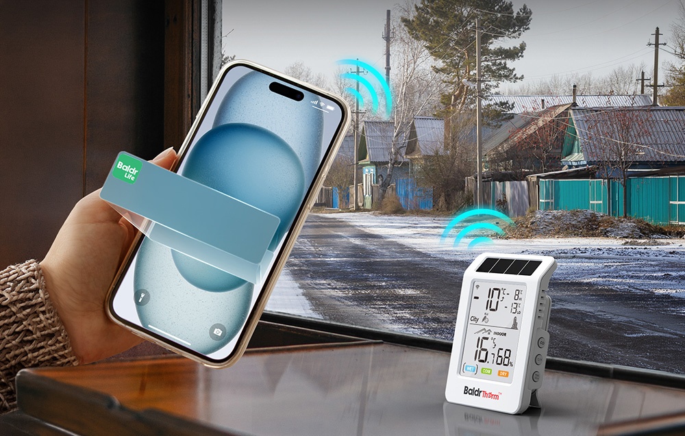 Ένα smartphone που κρατάει στο χέρι της· δίπλα του, πάνω σε ένα τραπέζι, ένα θερμοϋγρόμετρο BALDRTHERM