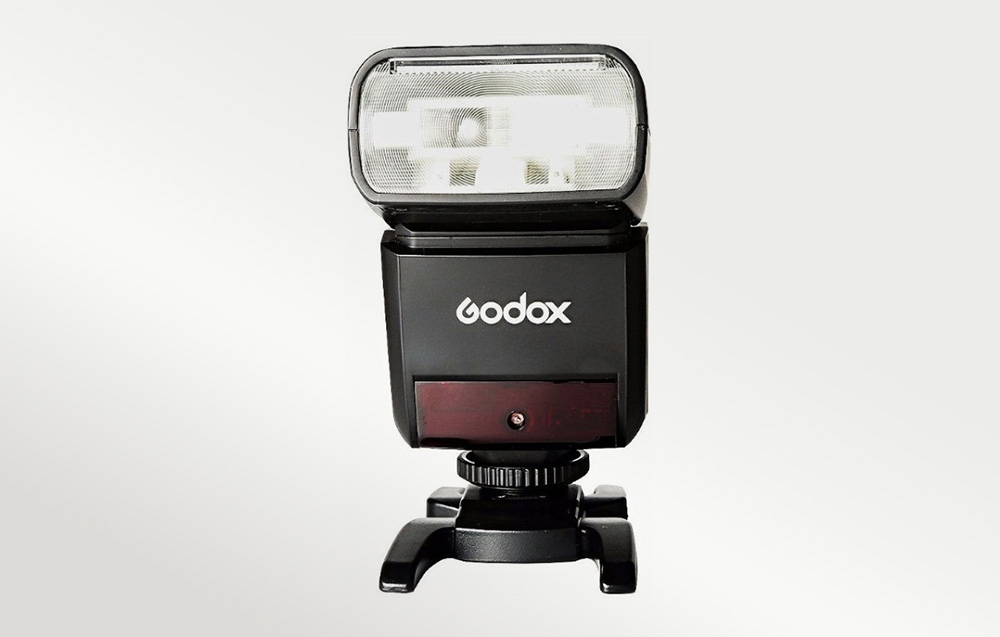 Φλας Godox TT350 σε βάση, μπροστινή όψη της κεφαλής του φλας, λογότυπο κατασκευαστή και κόκκινο πάνελ υποβοήθησης AF