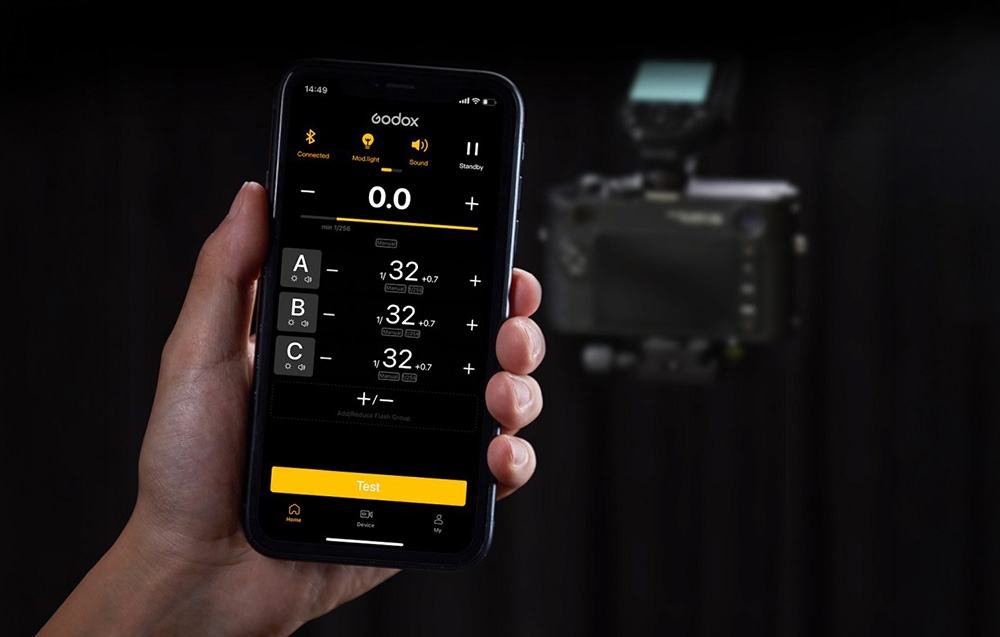 Ένα smartphone με ανοιχτή την εφαρμογή Godox Flash για τον έλεγχο των φλας, που κρατιέται στο χέρι με φόντο μια φωτογραφική μηχανή